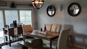 A dining area with a wooden table, cushioned chairs, and a hanging light fixture.