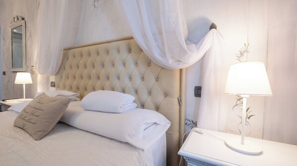 A neatly made bed with white linens and a tufted headboard, a bedside lamp, and a bedside table with a lamp.