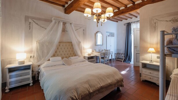 A bedroom with a large bed, a desk, and a chair. There is a chandelier above the bed and a window with curtains. - IL CASTAGNOLO COUNTRY B&B Torre Ardinghelli (San Gimignano)
