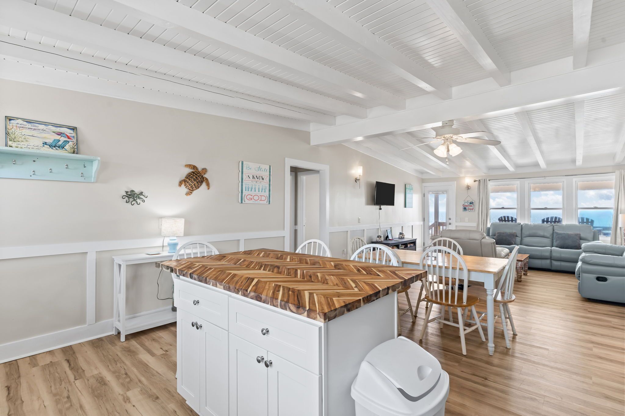 A spacious living area with a wooden island, white furniture, and a view through large windows.