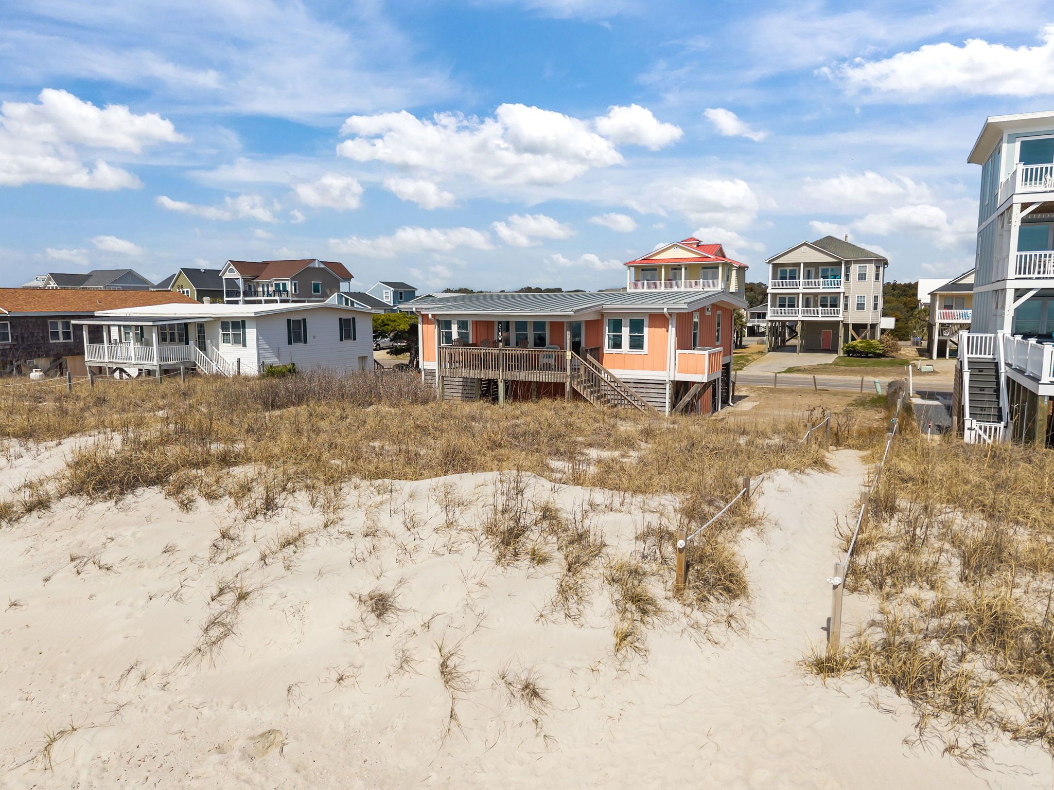 A beachfront property with multiple houses, including a two-story building with a red roof and a white building with a balcony.