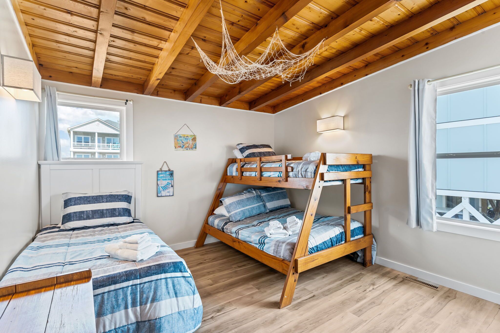 Ein gemütliches Schlafzimmer mit einem Etagenbett, einem Einzelbett, Holzbalken an der Decke, einer Hängematte und einem Fenster mit Blick auf ein Haus.