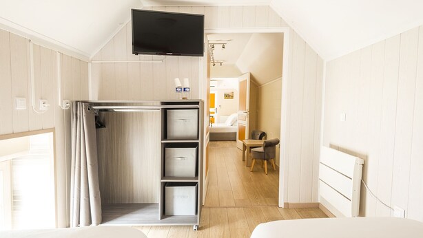 Ein Hotelzimmer mit Bett, Wandfernseher, Duschbereich und einer kleinen Sitzecke mit Tisch und Stuhl.