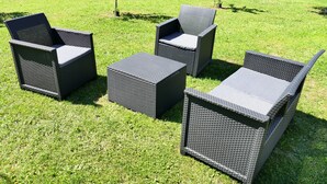 Ein Set aus Gartenmöbeln aus Rattan mit Kissen, auf einer grünen Rasenfläche platziert.