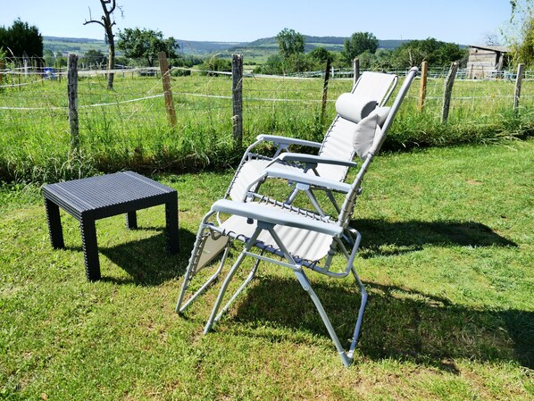 Un espace extérieur verdoyant, avec une chaise en métal et une petite table, le tout entouré d’une clôture en fil de fer.