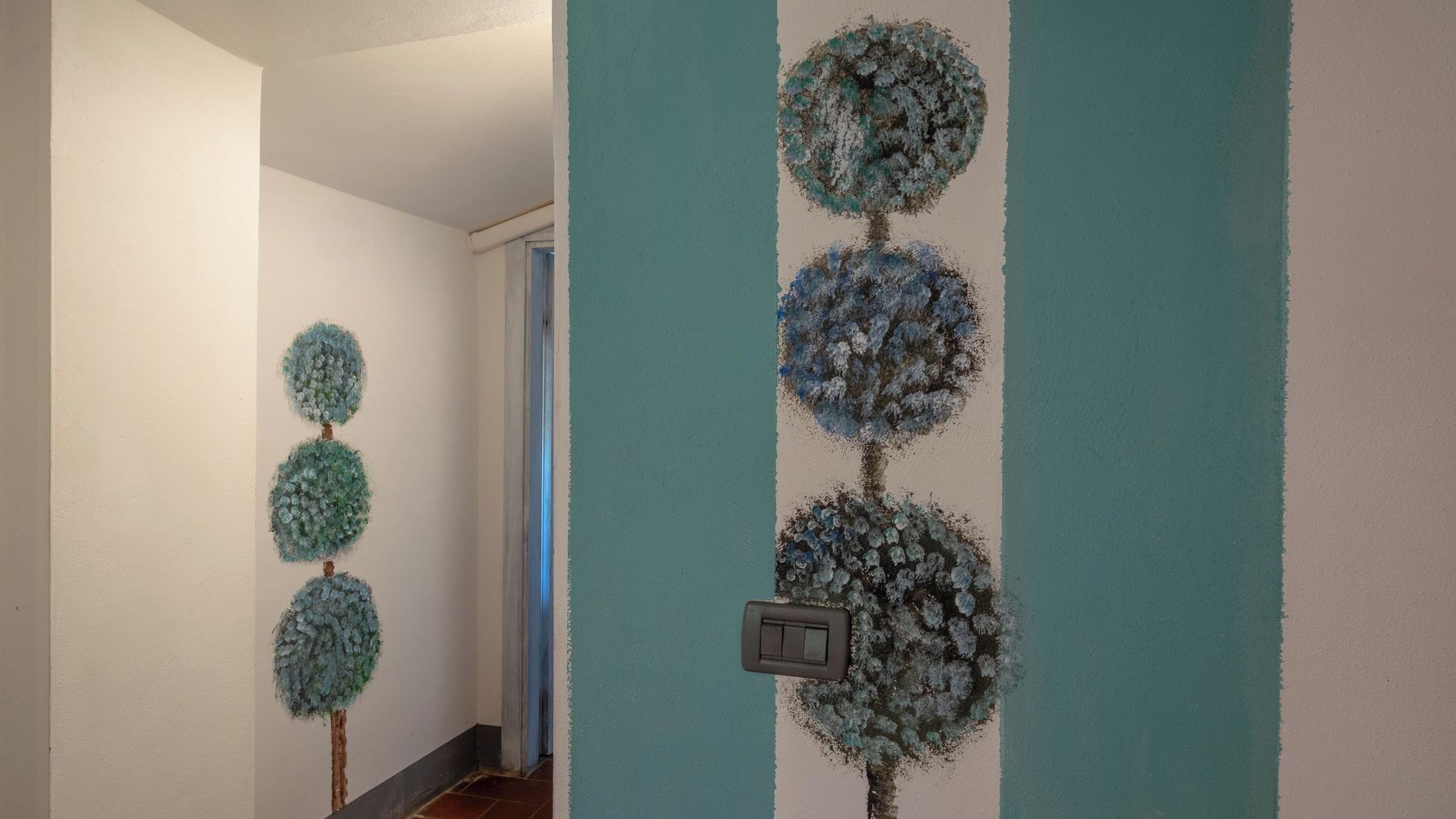 Un pasillo con pared de color claro y una franja azul turquesa. Se observan tres adornos esféricos en la pared, con superficie texturizada.