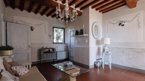 Una sala de estar con un sofá, una mesa de centro de vidrio, una araña, una chimenea y una ventana con vistas a árboles.
