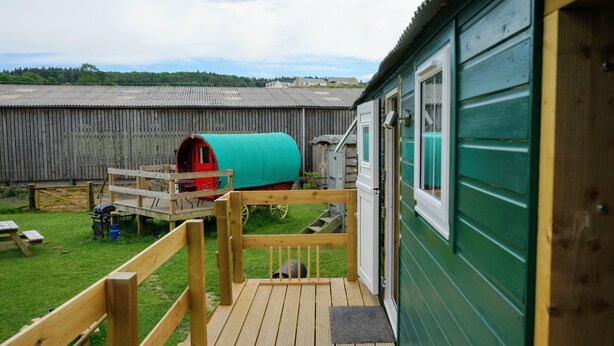 A wooden deck with a barbecue area, a green shed, and a red barrel in a backyard. - Unique Upcycled Straw Trailer @ Westcote (Hawick)