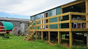 A two-story wooden building with a covered porch and a staircase leading to the upper level. - Unique Upcycled Straw Trailer @ Westcote (Hawick)