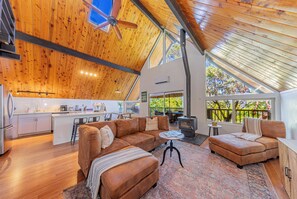 Un salón amplio con techo de madera, chimenea y un ventanal grande con vistas a la vegetación.