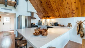 A modern kitchen with a large island, wooden stools, stainless steel appliances, and a high wooden ceiling. - Oakhurst Cabin|Bass Lake View|Game Room|Hot Tub! (Oakhurst)