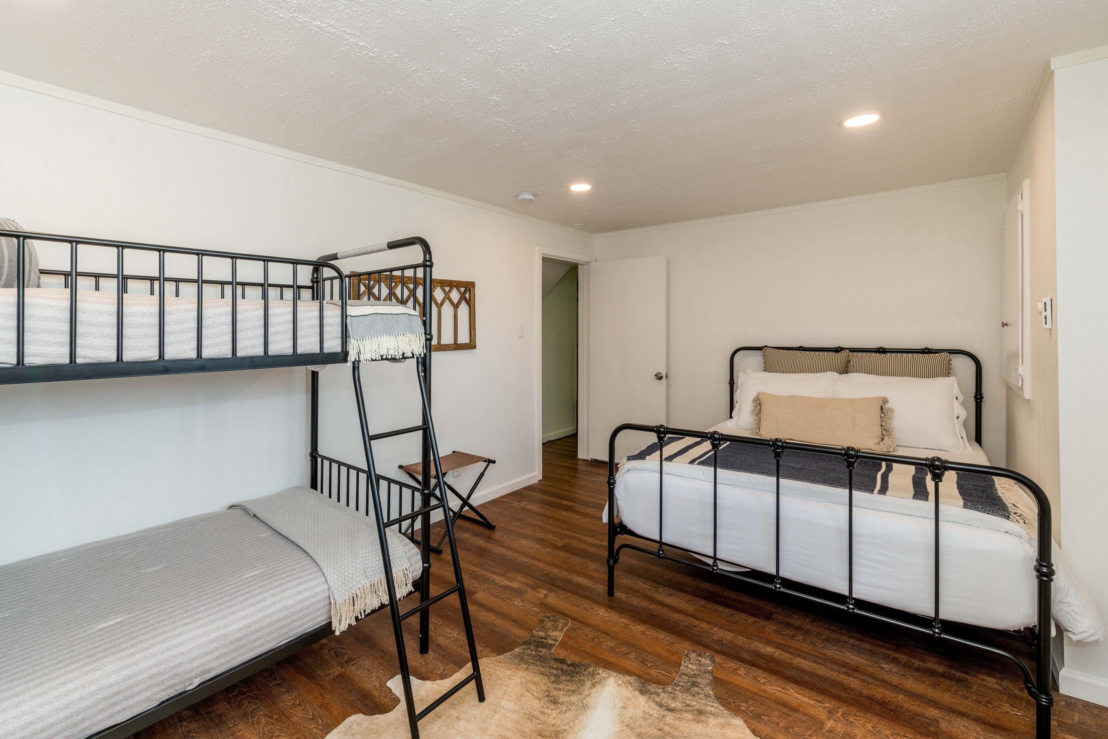 A room with bunk beds, a single bed, wooden flooring, and a door leading to another room.