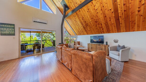 A spacious living area with a high wooden ceiling, a large leather sofa, a grey armchair, and a television on a wooden cabinet. - Oakhurst Cabin|Bass Lake View|Game Room|Hot Tub! (Oakhurst)