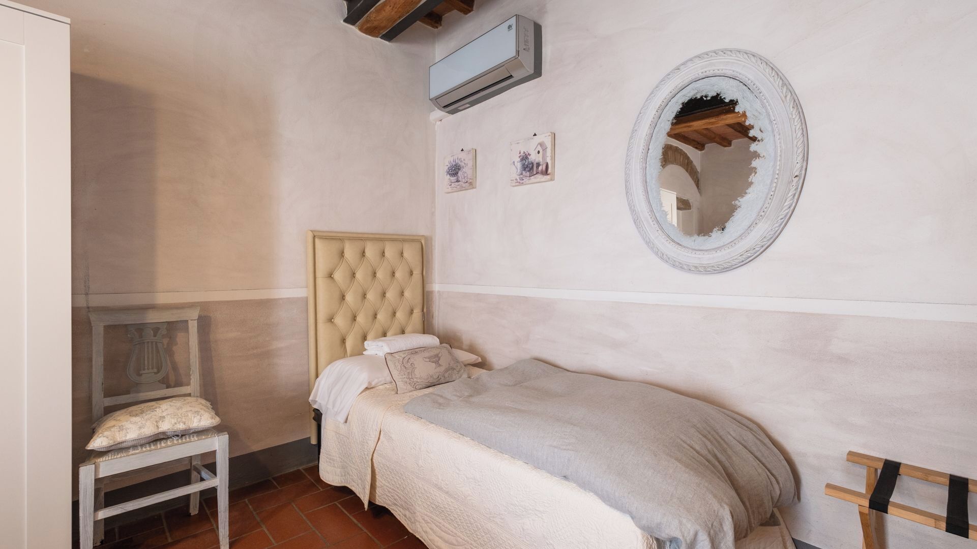 Ein kleines, gemütliches Schlafzimmer mit einem Einzelbett, einem Holzstuhl, einem Spiegel und einem kleinen Tisch.