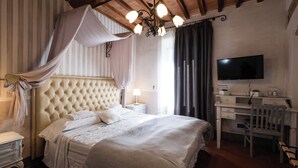 A bedroom with a tufted headboard, a bed with white linens, a desk with a chair, a television, and a chandelier. - IL CASTAGNOLO COUNTRY B&B Torre Chigi (San Gimignano)