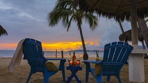 Two blue chairs and a small table with a bottle and candle on a beach at sunset. - Casa Caracol (Bucerías)
