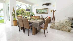 A dining area with a table set for six, surrounded by wicker chairs, a potted plant, and a large window offering a view of the outdoors. - Casa Caracol (Bucerías)