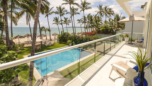 A balcony with a pool, palm trees, and a view of the beach. - Casa Caracol (Bucerías)