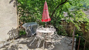 Une terrasse avec une table et des chaises, un barbecue couvert et un parasol rouge.