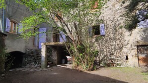 Une ruelle étroite aux murs de pierre, surmontée d’une petite arche, et un arbre qui offre de l’ombre.