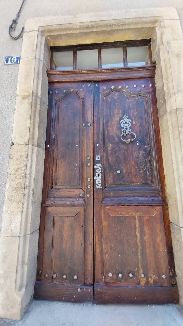 A large wooden double door with a metal handle and decorative elements, set in a stone wall with a number '19' sign above.