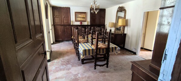 A dining area with a hexagonal tiled floor, wooden chairs with patterned tablecloths, a chandelier, and a mirror above a dresser. - Large 200 m² house with a garden, terraces, and a courtyard. Florac Center. (Florac-Trois-Rivières)