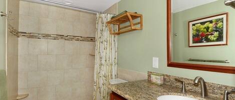 A bathroom with a shower, toilet, vanity with a sink, and a mirror.