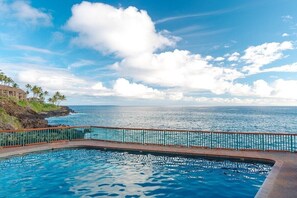 Ein Pool mit Blick auf das Meer und ein Gebäude im Hintergrund.