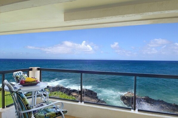 Ein Balkon mit Tisch und Stühlen mit Blick auf eine felsige Küste und das Meer.