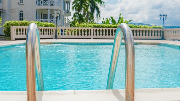 A swimming pool with metal railings, surrounded by a white fence and lush greenery. - Mira Bay Apartments (Montego Bay)