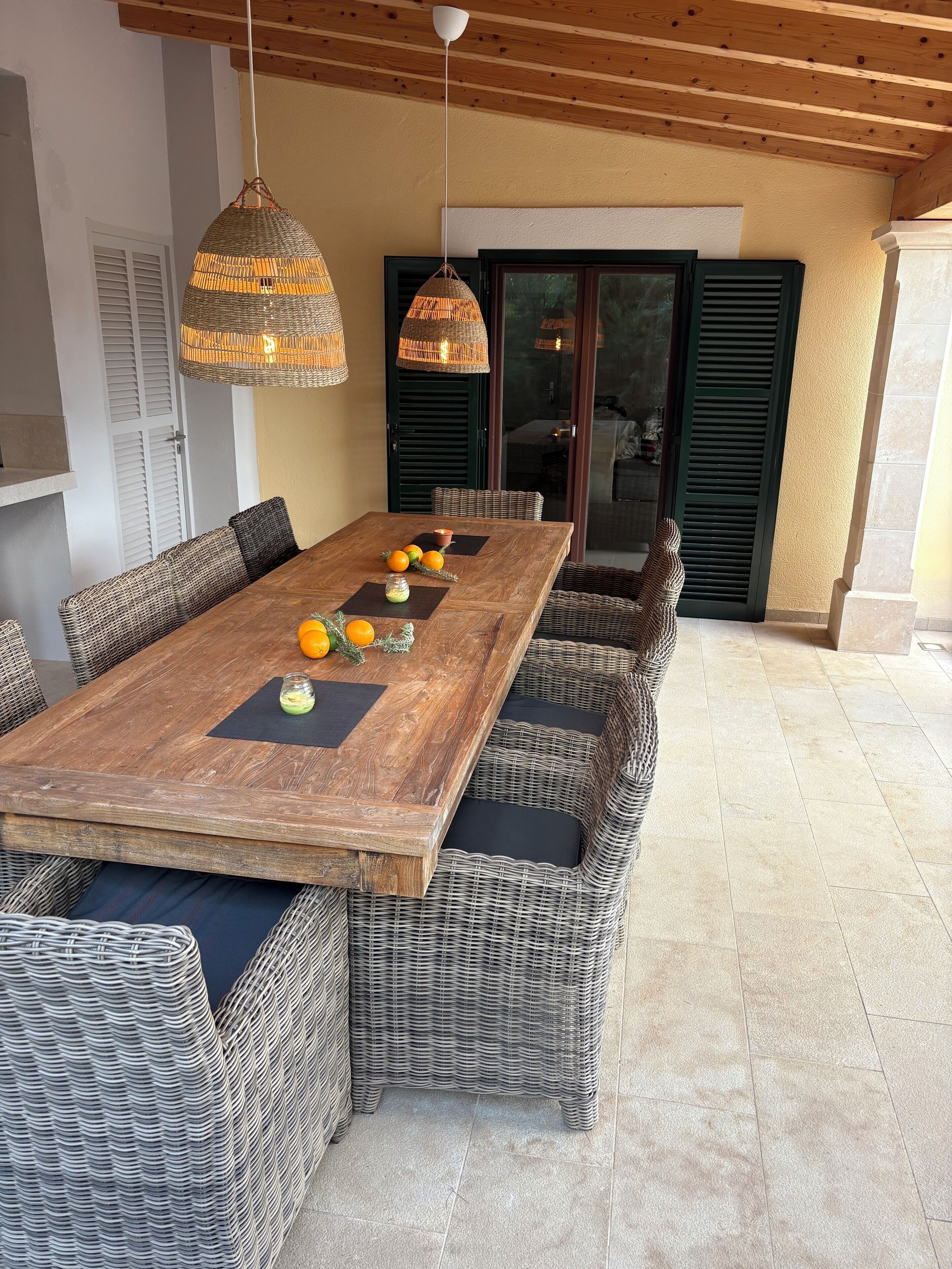 Una mesa de comedor de madera, sillas de mimbre, una lámpara colgante de mimbre y vistas al exterior.
