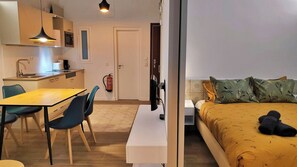 Une pièce de taille modeste comprenant un lit, un bureau, des chaises, un coin cuisine et un extincteur.