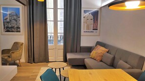 Un salon meublé comprenant un canapé, un fauteuil, une petite table et une porte-fenêtre donnant sur un balcon.