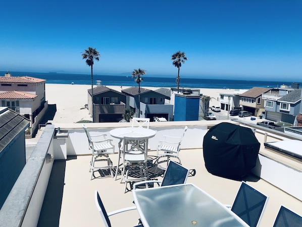 Un balcón con mesa y sillas que da a una playa con palmeras y casas.