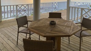 A covered outdoor area with a wooden table and wicker chairs, overlooking a beach and ocean at sunset. - Beautiful Casa Sol  (Great Harbour Cay)