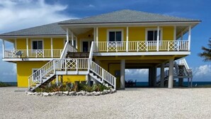 A two-story yellow building with a balcony, a staircase, and a view of the ocean. - Beautiful Casa Sol  (Great Harbour Cay)