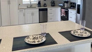 A modern kitchen with white cabinets, a stainless steel refrigerator, and a central island with two plates and a glass. - Beautiful Casa Sol  (Great Harbour Cay)