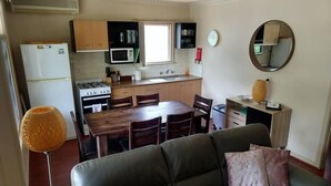 En kompakt bolig med tekøkken, spiseplads og opholdsområde med sofa og stole.