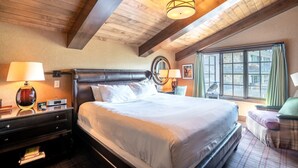 A bedroom with a large bed, wooden ceiling beams, a window with a view, and a bedside table with a lamp. - Western Cowboy Quarters steps away from Vail Gondola w/ Hot tub  and  Spa access (Vail)