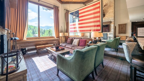 A spacious living room with a large window offering a mountain view, a fireplace, and a large American flag. - Western Cowboy Quarters steps away from Vail Gondola w/ Hot tub  and  Spa access (Vail)