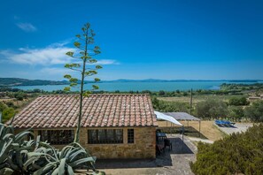 A stone building with a tiled roof, a patio with a table and chairs, and a view of a lake and hills.