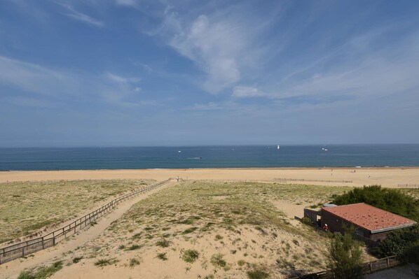 Une vue sur la plage, avec un sentier bordé de clôtures menant à un bâtiment doté d’un toit rouge.