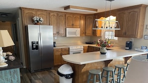 Una cocina con armarios de madera, electrodomésticos de acero inoxidable, una isla central con taburetes y un bote de basura.