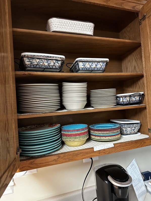 Un mueble de cocina con estantes que contienen varios platos y una cafetera Keurig.