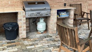 An outdoor grill station with a brick base, a gas tank, and a table with chairs. - Milgate Motel (Casino)