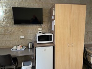 Una kitchenette equipada con microondas, un refrigerador pequeño, cafetera y televisor montado en la pared.