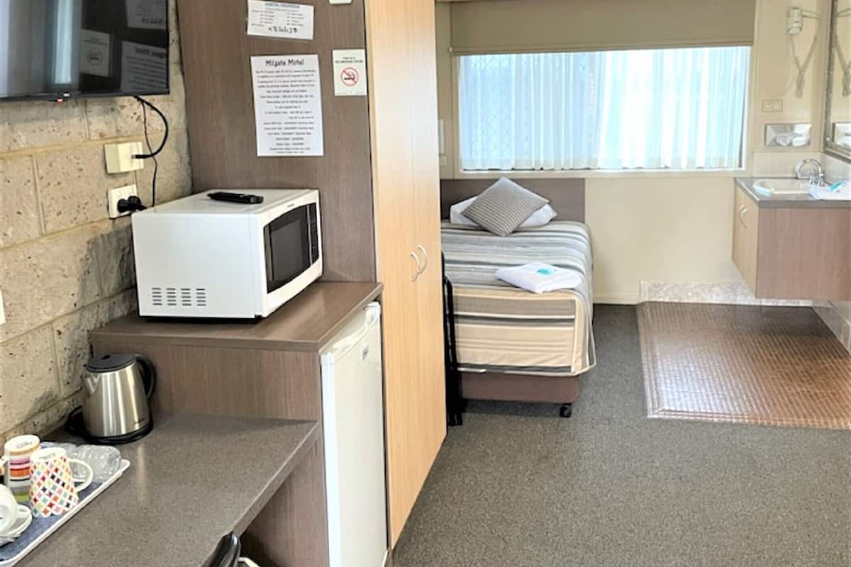 A compact hotel room with a kitchenette, a bed, a TV, and a window.