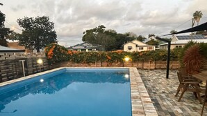 Piscina rectangular con borde de piedra, rodeada de un patio con mesa y sillas.