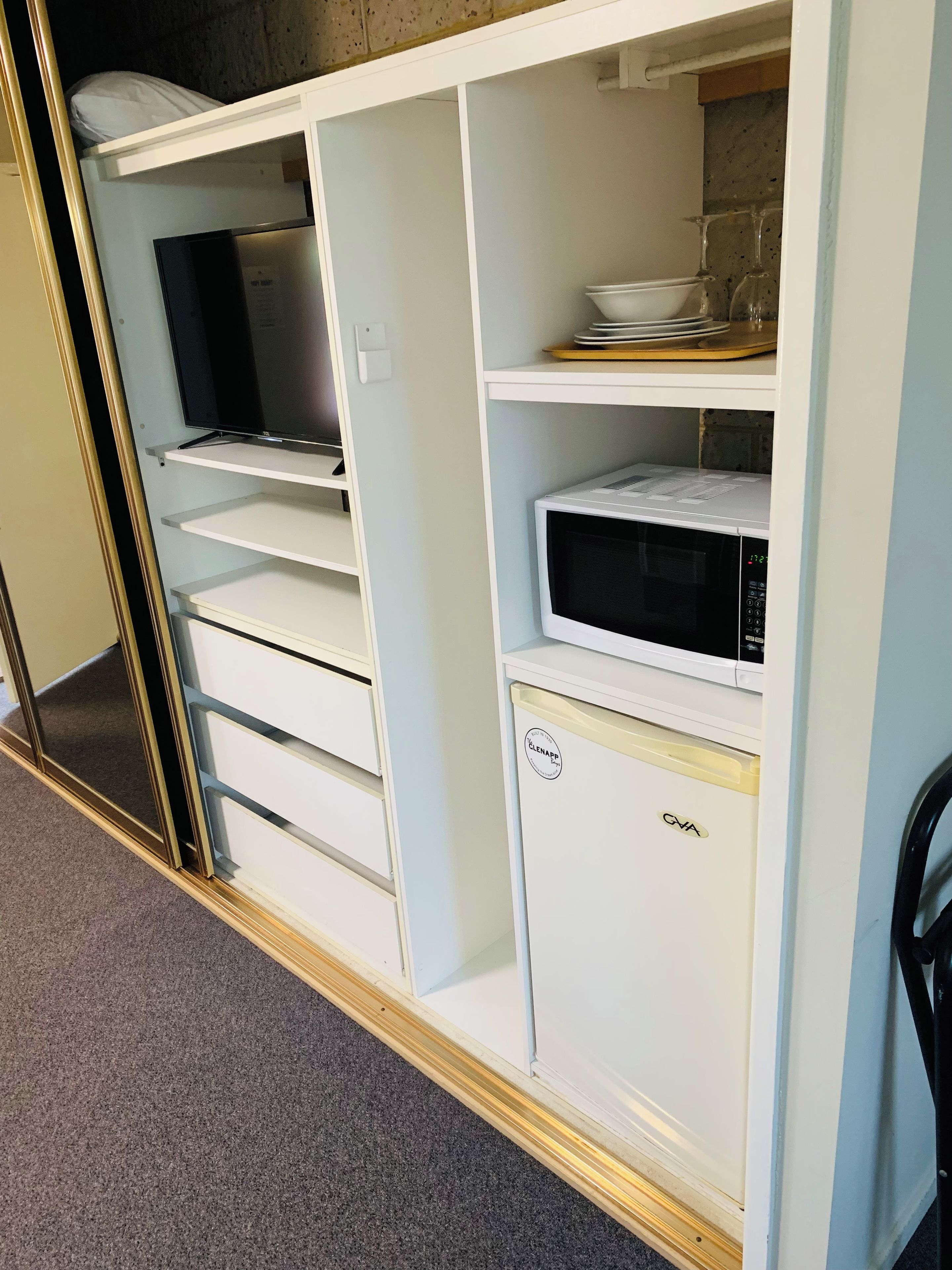 Un depósito de almacenamiento blanco con un microondas, un televisor y un mueble pequeño.