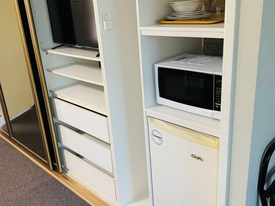 A white storage unit with a microwave, a television, and a small cabinet.